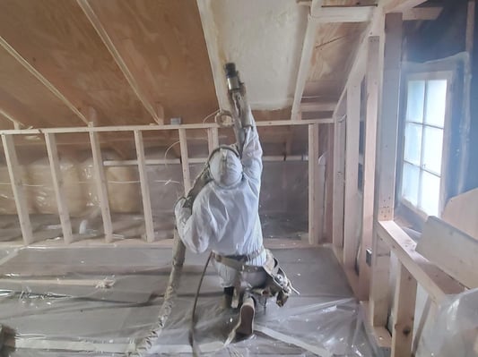 A spray foam insulation contractor installing closed cell in an attic. This overhead spraying will create an encapsulated attic.