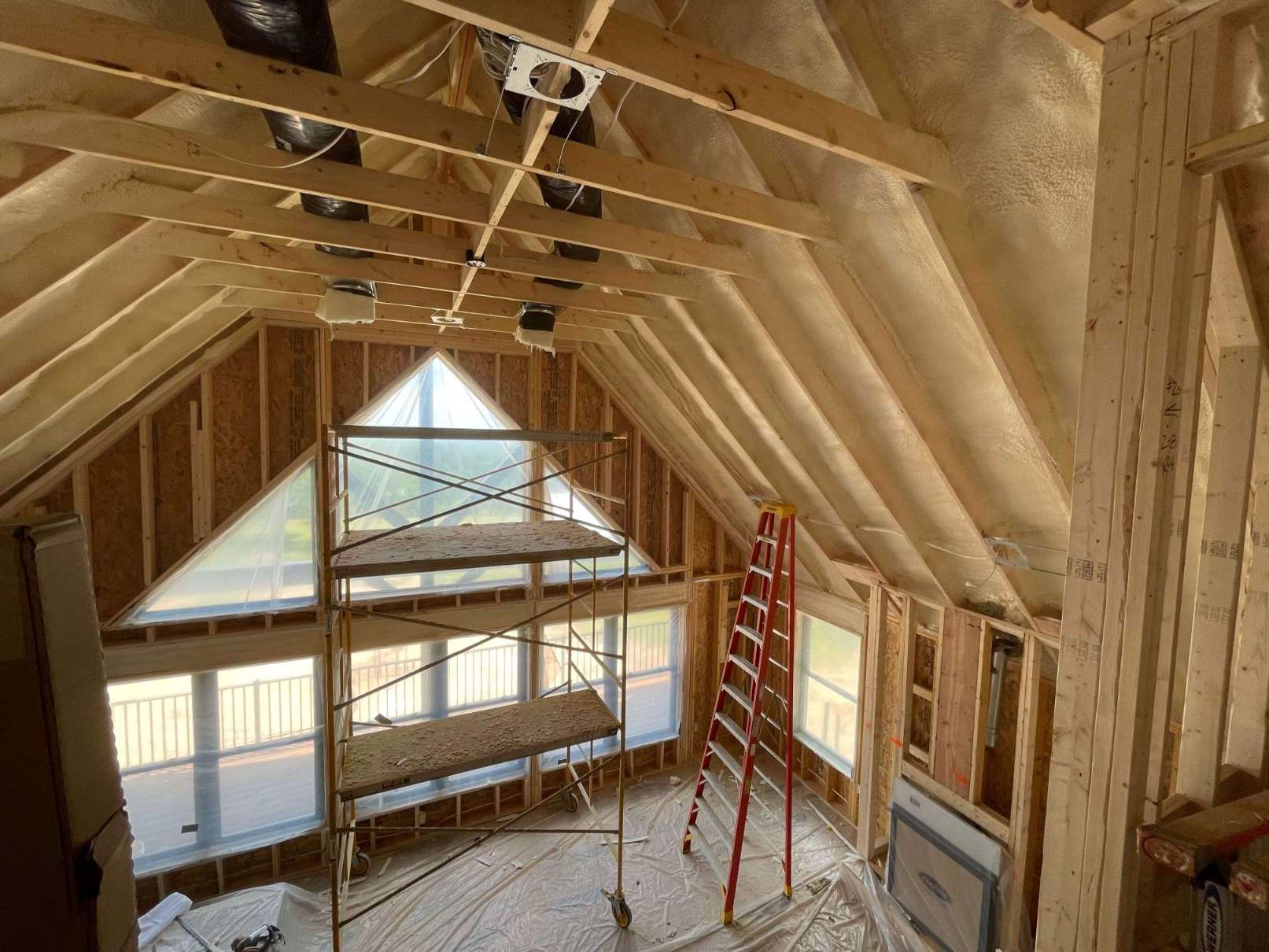 A new construction home, the underside of its roof insulated with closed cell spray foam. Accessibility aids like scaffolding and ladders are visible.
