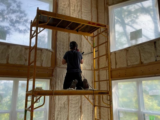 A spray foam insulation crew member shaving excess open cell spray foam from the walls of a new construction home.