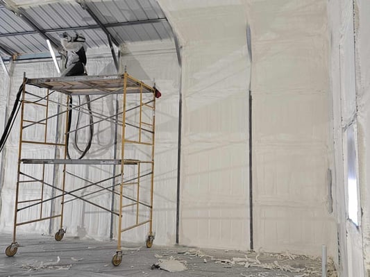 A spray foam installer insulating the metal roof of a pole building with closed cell spray foam insulation.