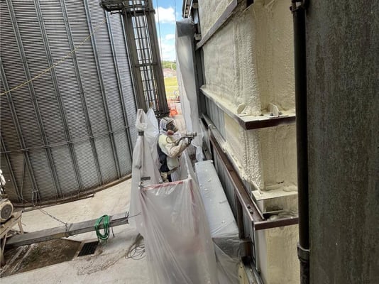 A spray foam insulation contractor installing closed cell spray foam on the exterior of a feed mill.